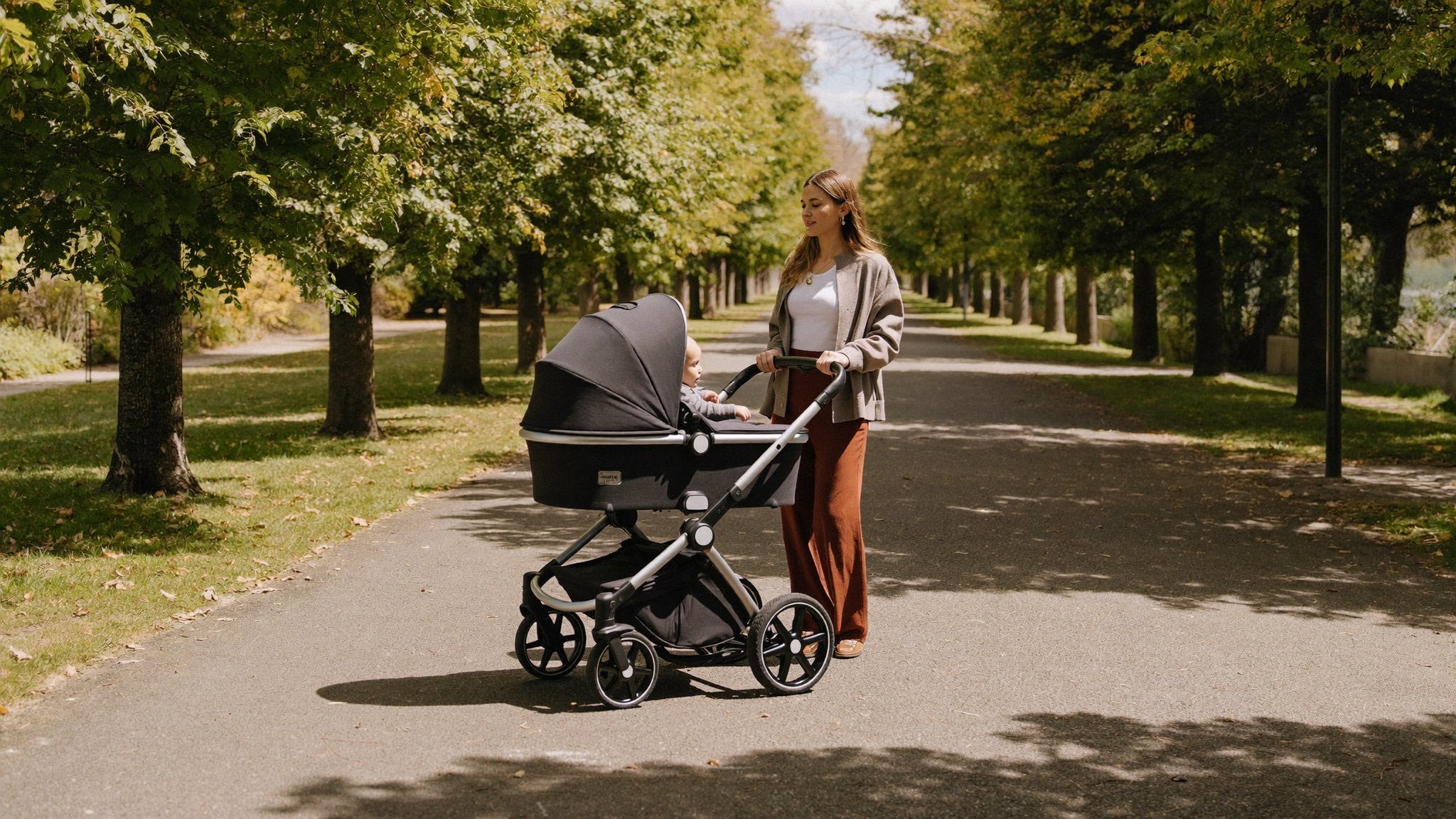 Mother walking with a 3-in-1 baby travel system pram along a tree-lined park path - Bambinos & Beyond 3-in-1 Travel Systems