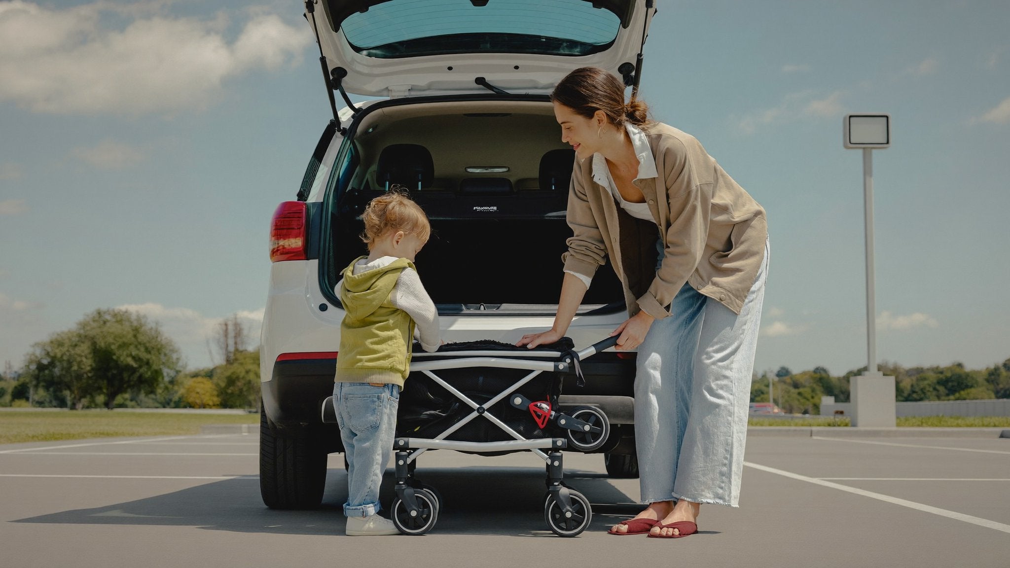 Mother folding a compact stroller by the car with her toddler - Bambinos & Beyond Compact Fold & Travel