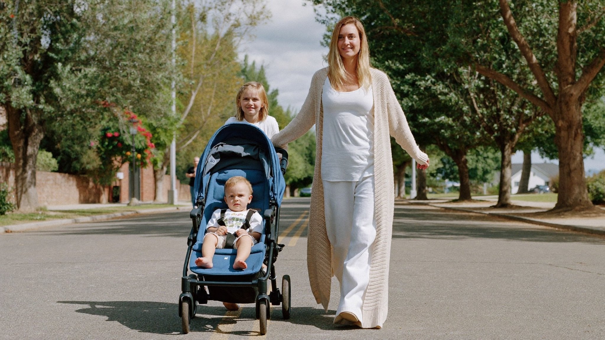 Mother walking with a double pushchair and two children - Bambinos & Beyond Double & Twin
